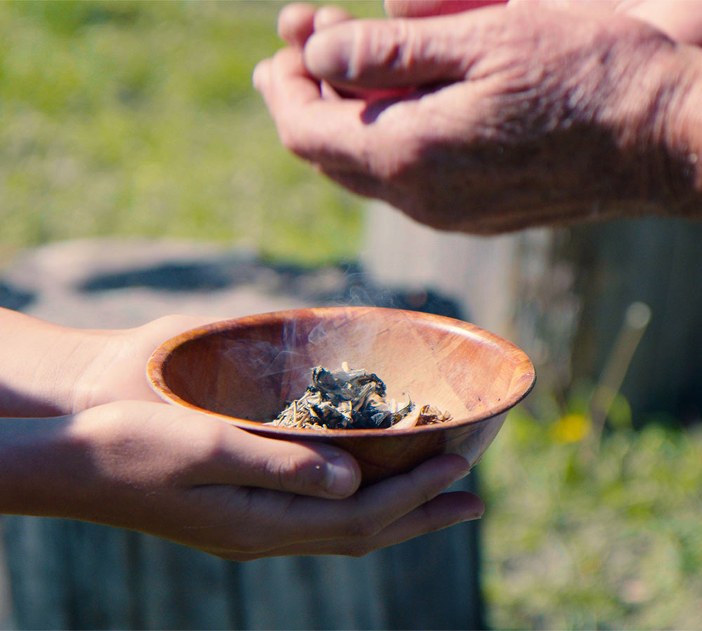 close up of hand holding burning sage in smudge bowl