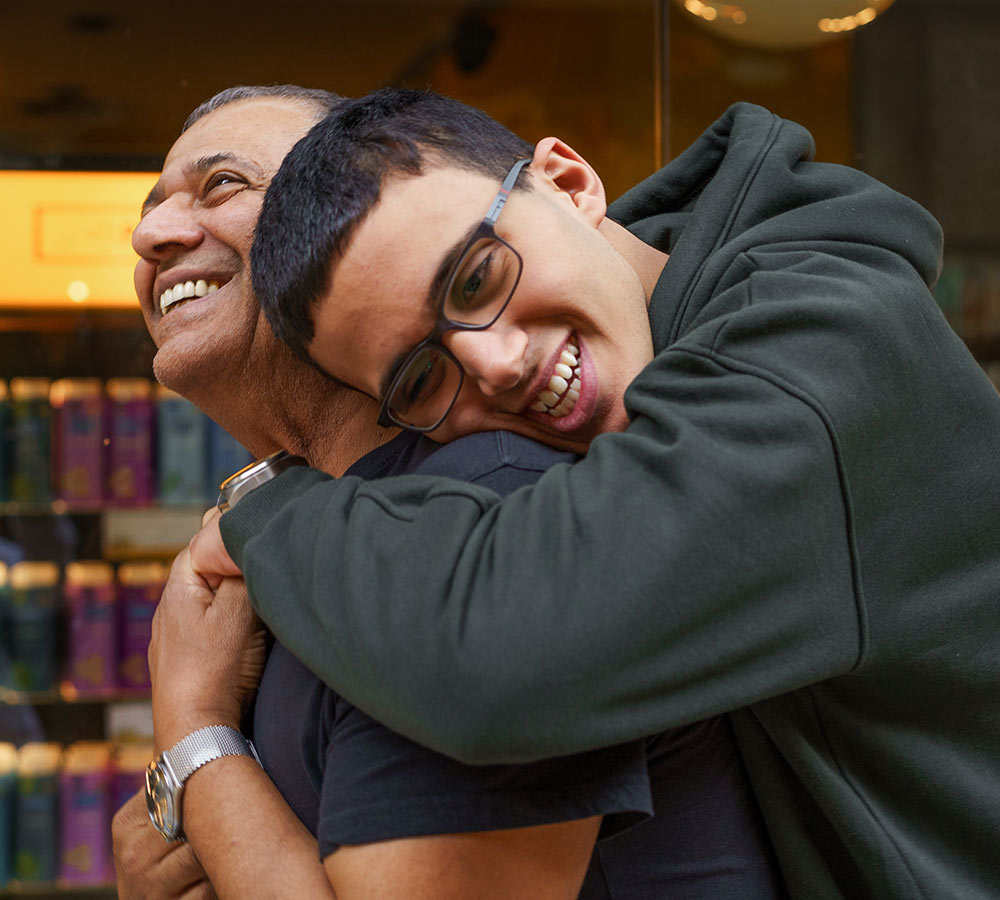 teen boy leans over to hug his father, who to be smiling at him