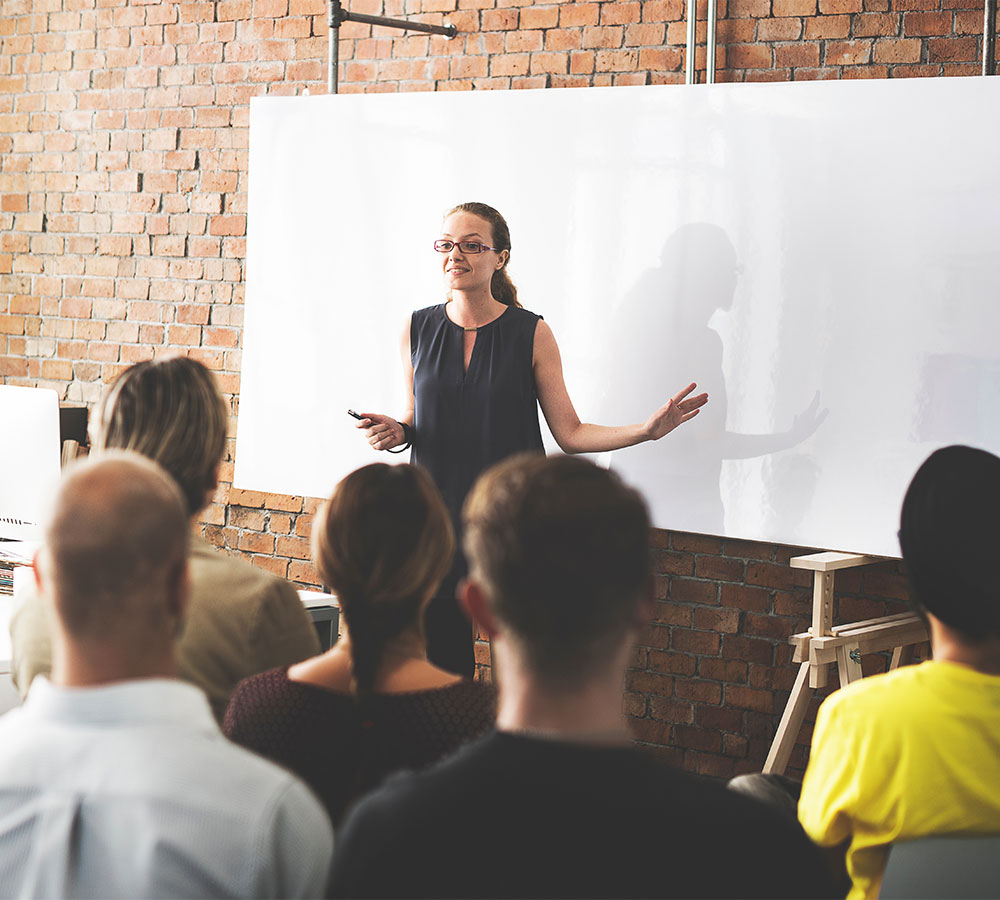 Woman standing in front of white board training a group of people seated listening